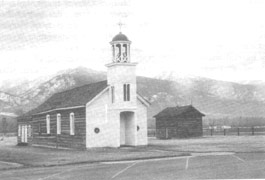 Small but beautiful church, beside a smaller log house, with mountains in bcakground