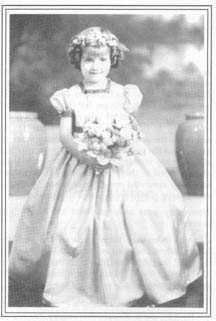 Marlene at age 4, holding flowers and wearing a white dress